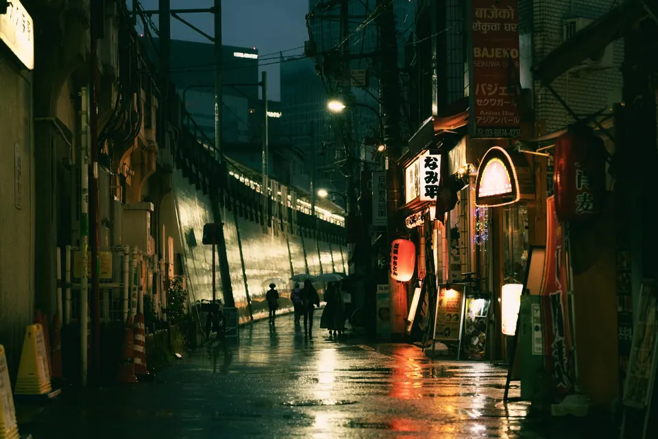 Wet back alley at night, warm light spilling from a doorway onto the paving