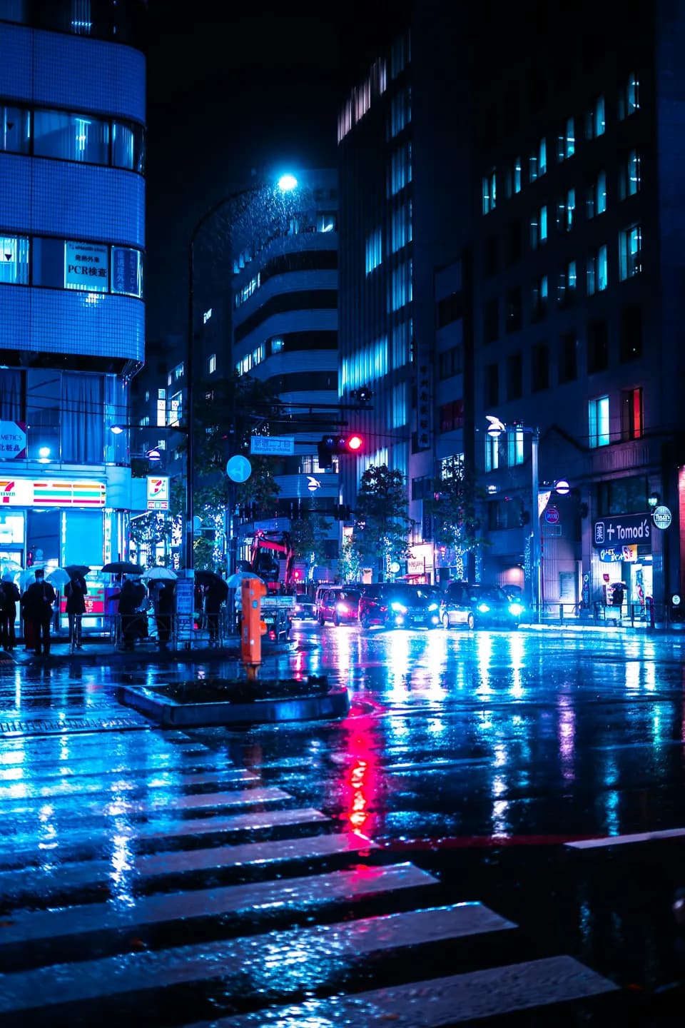 Blue-lit crossing at night, pedestrians stepping into the road under office towers