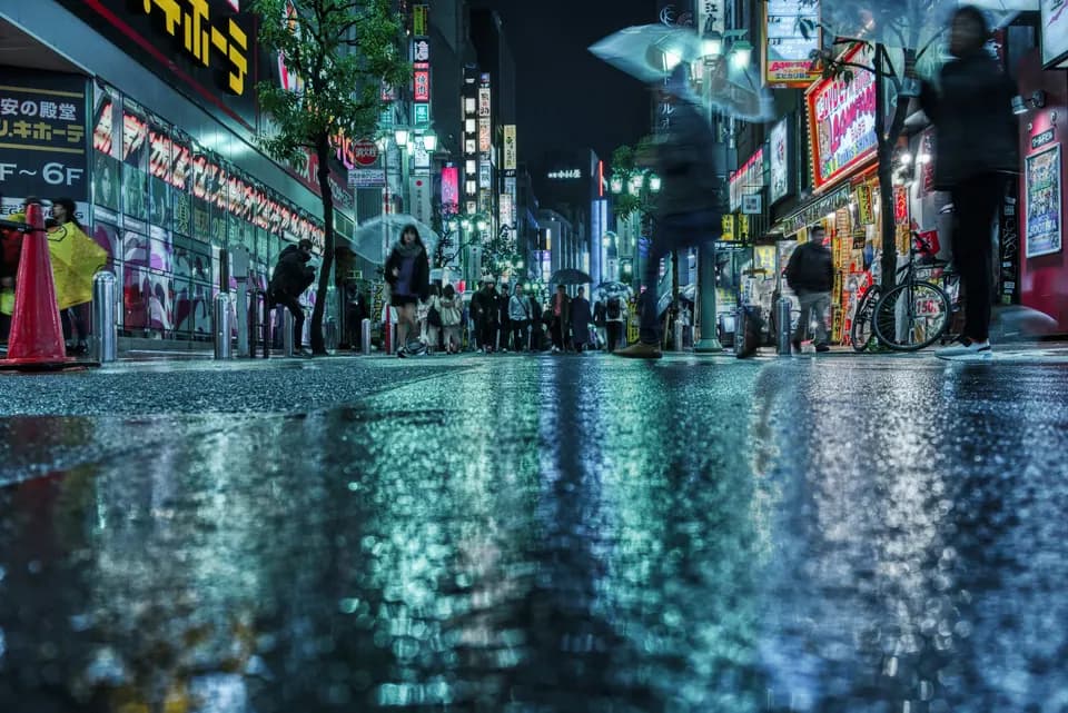 Low viewpoint across wet pavement, signage broken into coloured reflections underfoot