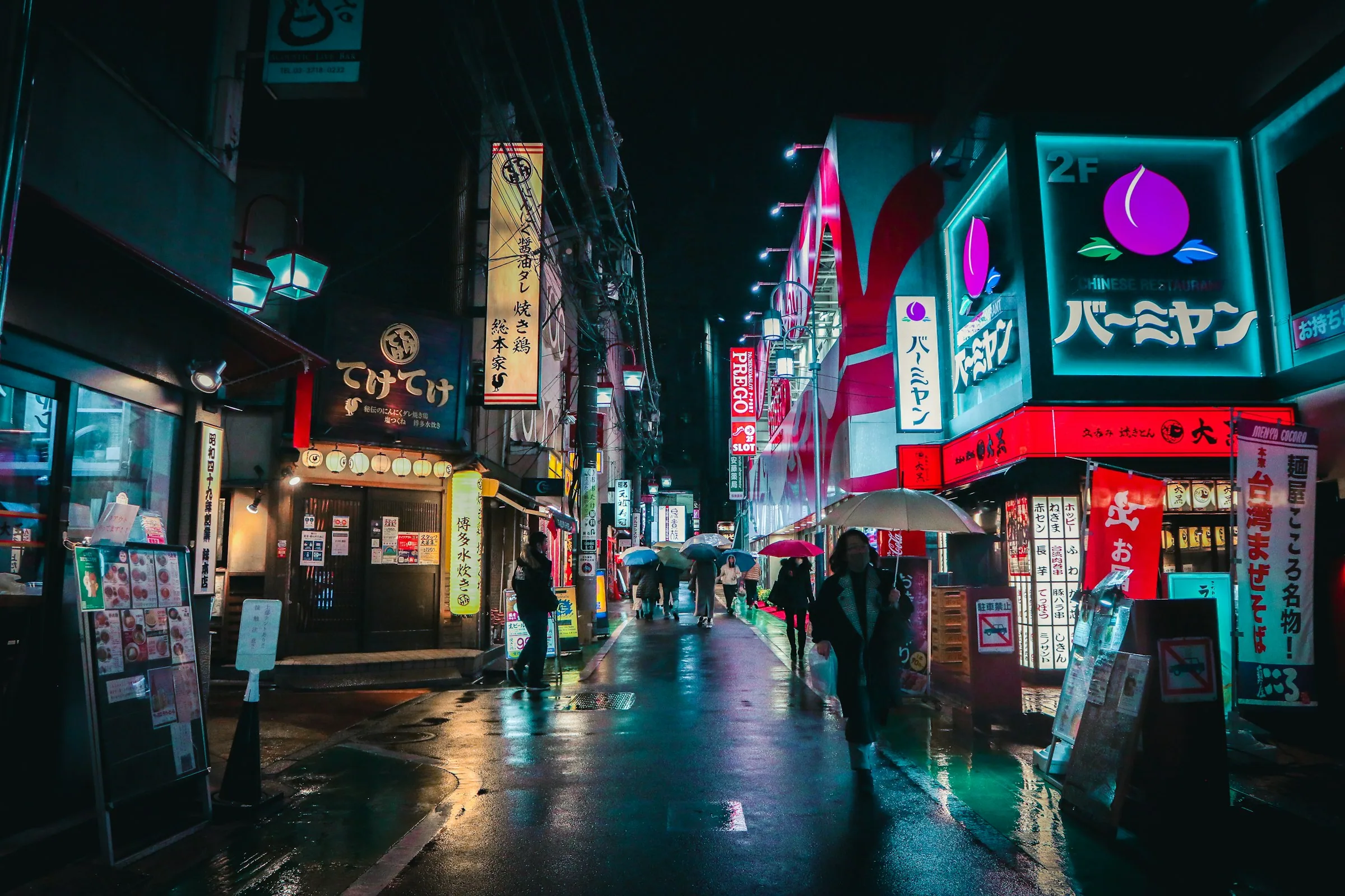 Rain-slick street at night, figures walking between lit shopfronts, signage stacked into the distance